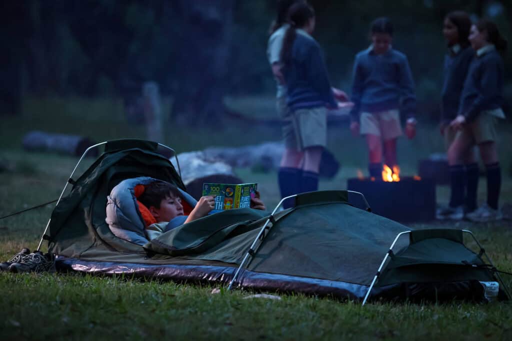 Tudor House student camping in a sleeping bag and reading a book