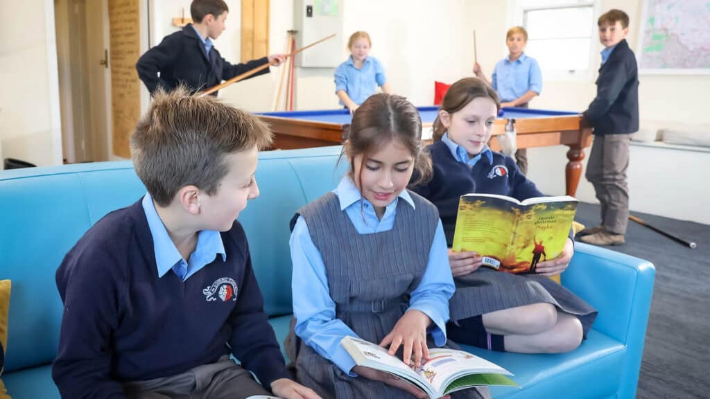 Tudor House boarding students in the common area, some students are reading books on the couch and others are playing pool behind