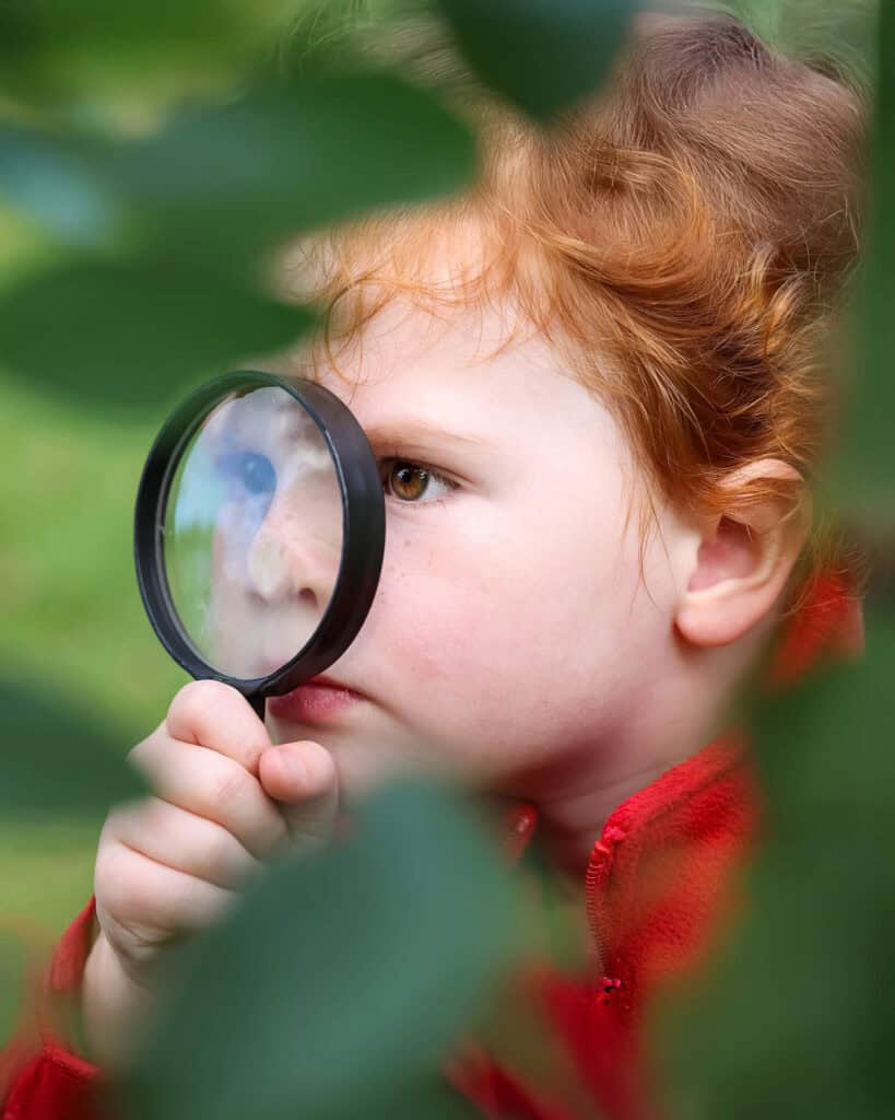 Tudor House pre-kindergarten student looking through a magnifying glass at leaves