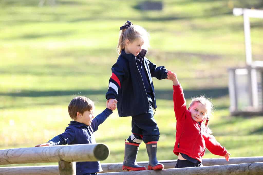 Tudor House pre-kindergarten student walking on a beam in gumboots with other students holding their hands