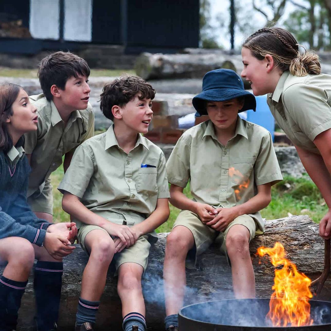 Tudor House students sitting on a log in front of a camp fire, chatting