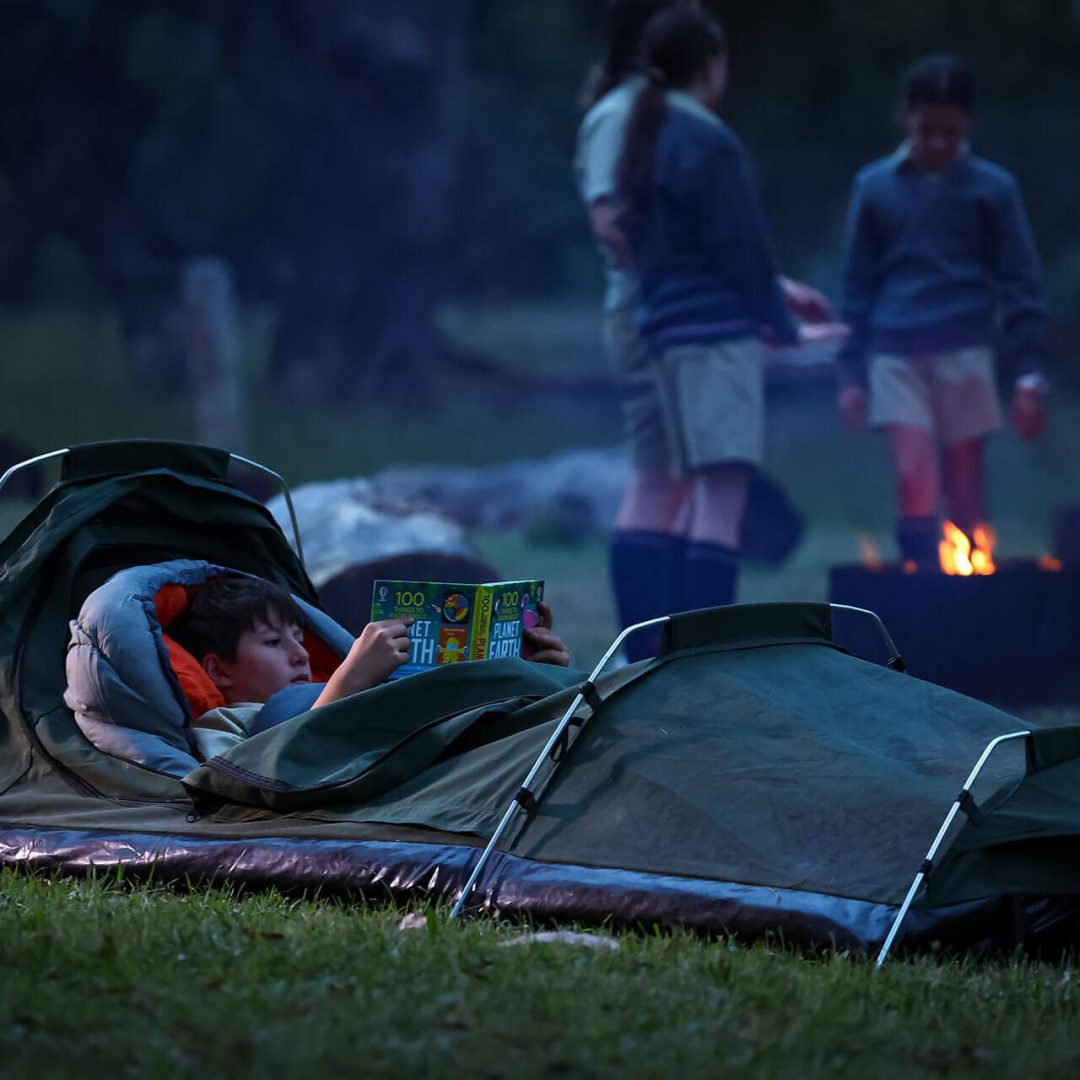 Tudor House student camping in a sleeping bag and reading a book